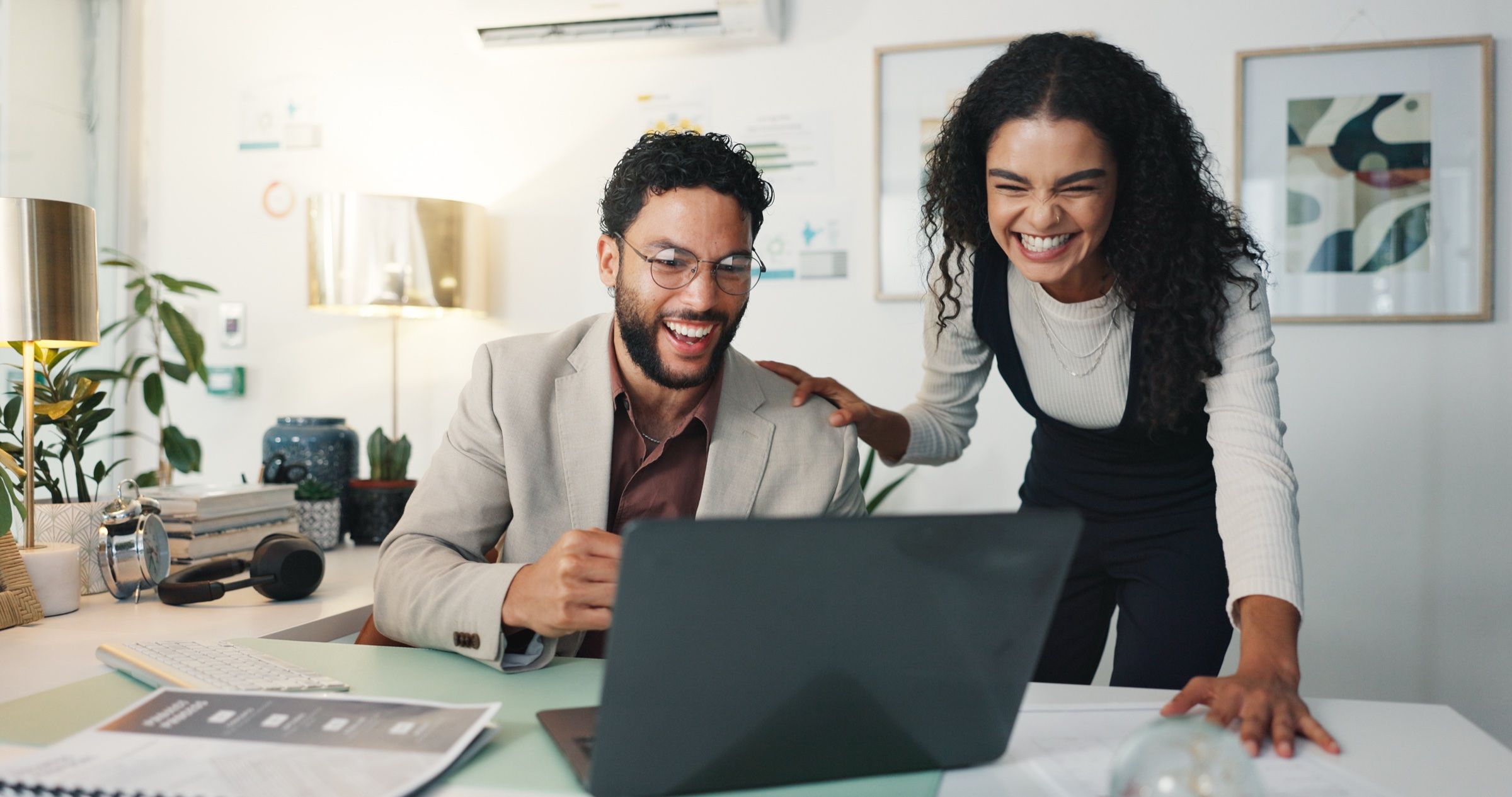 Un contador y una contadora celebrando frente a la laptop en la oficina de su despacho.